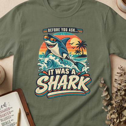 A cartoon shark wearing sunglasses surfs at sunset with text "Before you ask... It was a shark".