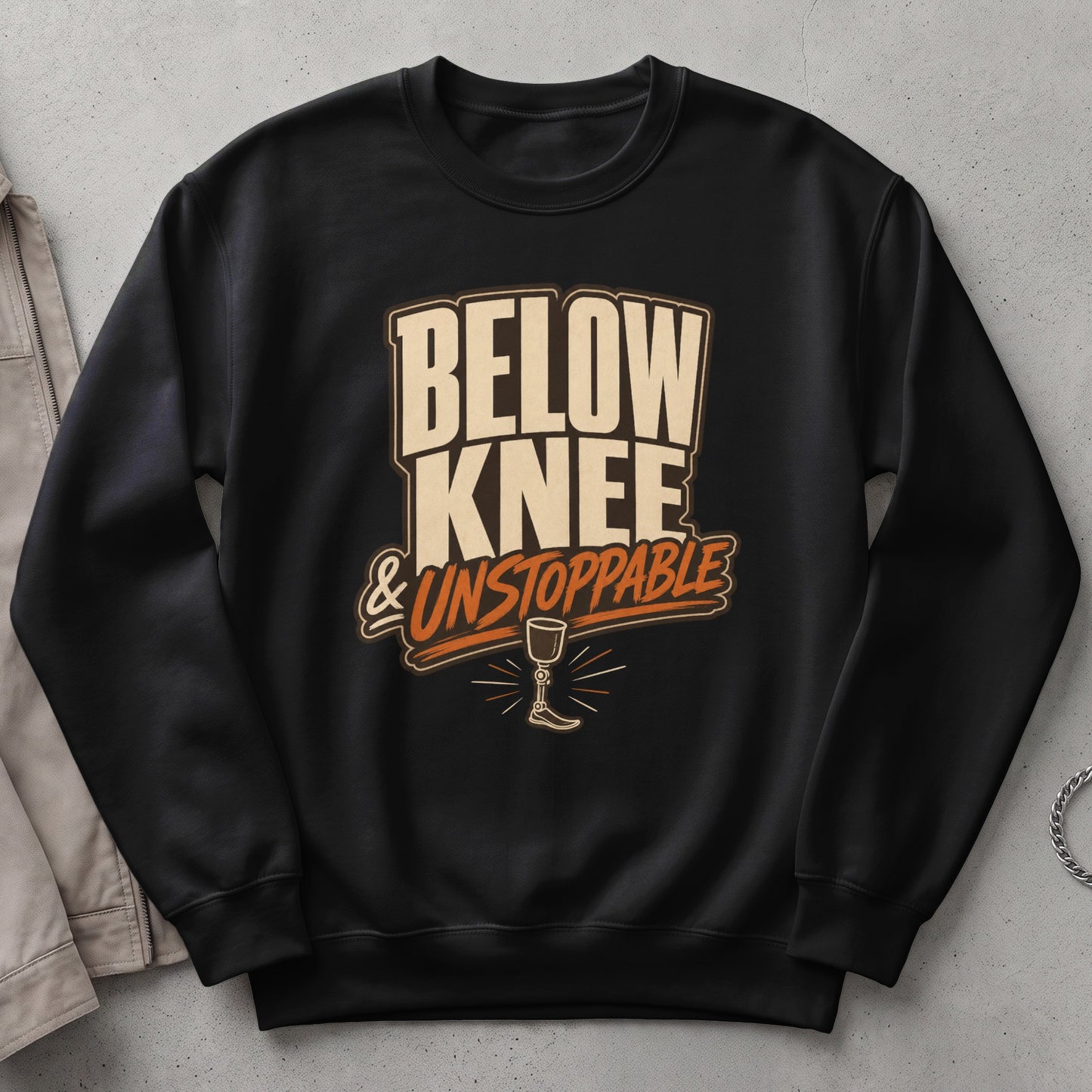 Black sweatshirt with "BELOW KNEE & UNSTOPPABLE" text and prosthetic leg graphic.