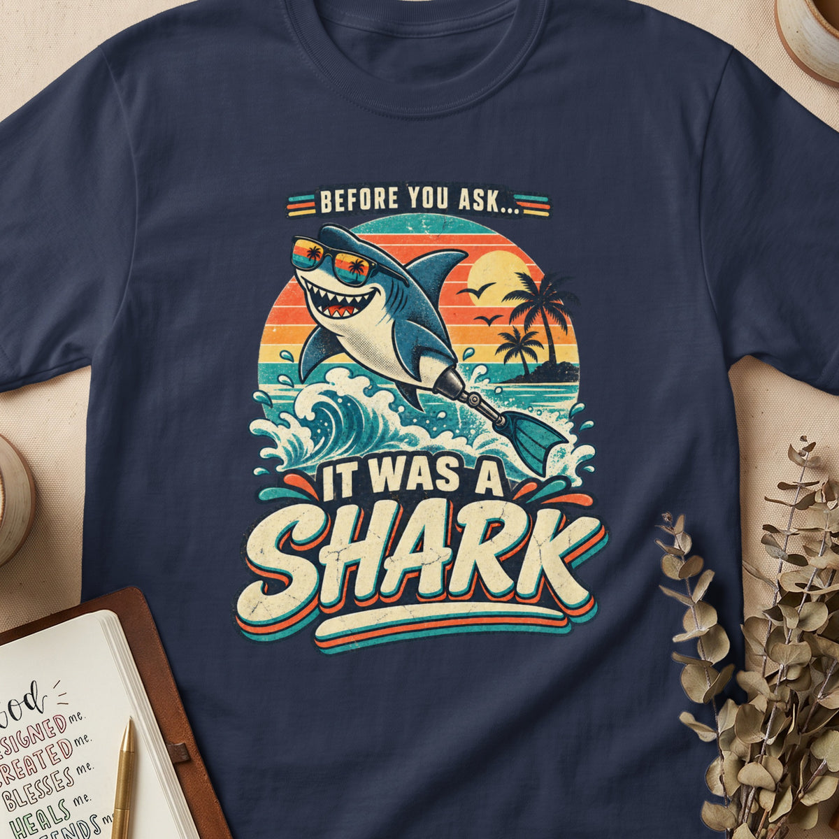 Retro graphic on a navy shirt: shark with sunglasses, waves, and "IT WAS A SHARK" text.
