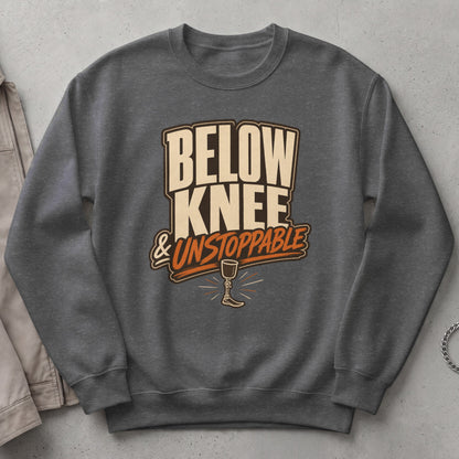 Dark grey sweatshirt with "Below Knee & Unstoppable" text and prosthetic leg graphic.