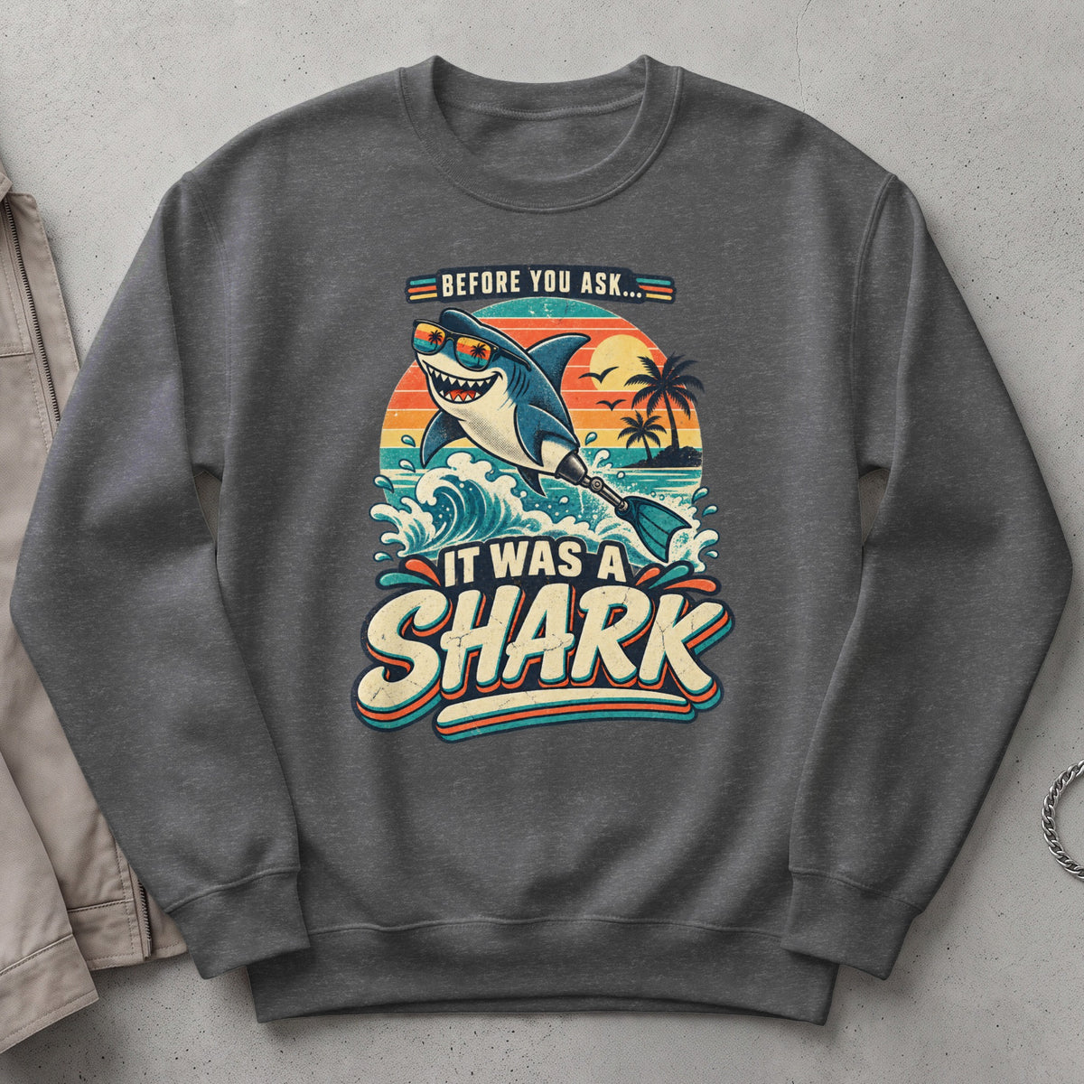 Graphic sweatshirt with a smiling shark wearing sunglasses saying "Before You Ask... It Was A Shark."