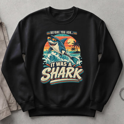 Black sweatshirt with "It Was A Shark" graphic featuring a smiling shark on a surfboard at sunset.