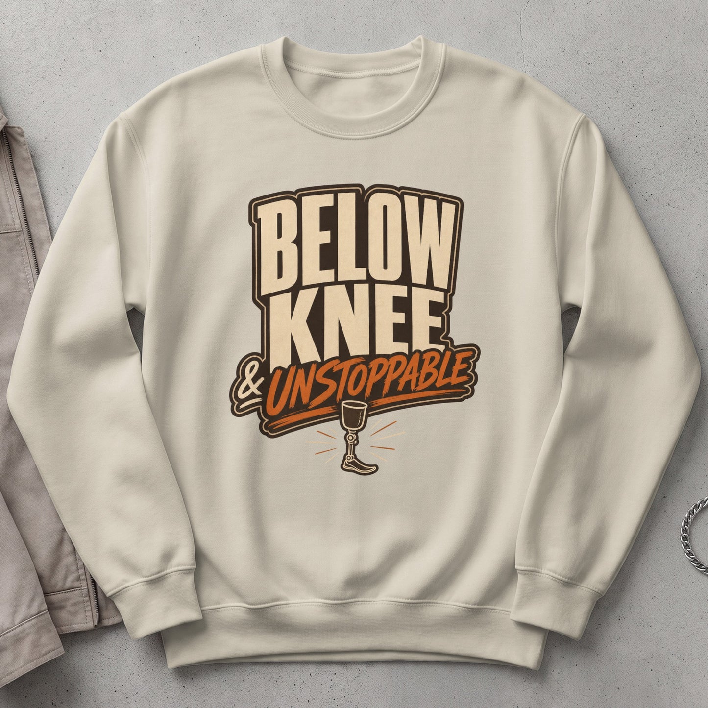 Cream sweatshirt with "Below Knee & Unstoppable" graphic and prosthetic leg.